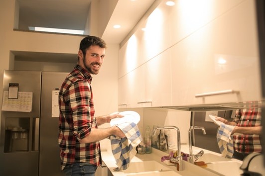 a man doing the dishes with a smile, accepting this chore