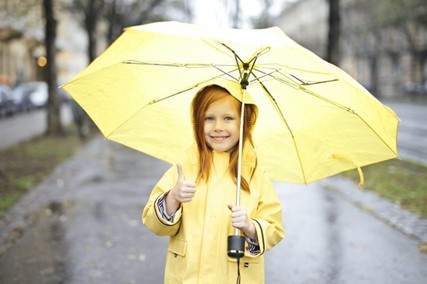 A girl with an umbrella accepting the rain with a smile.