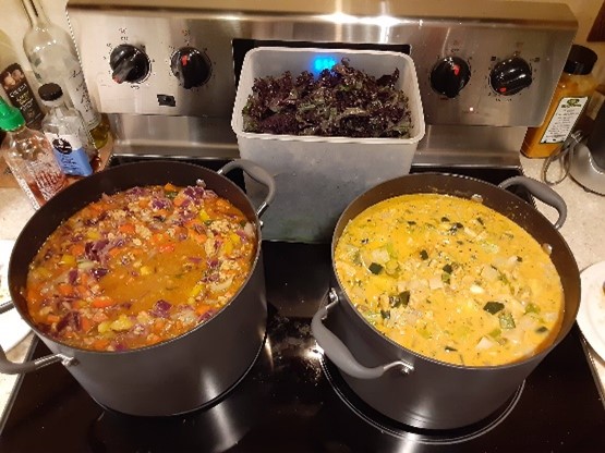 two different curries on the stovetop with a huge volume of greens waiting to be added