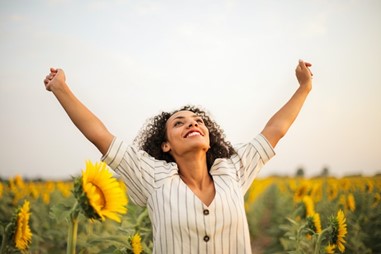 a woman in a field looking up with arms wide, in a power pose