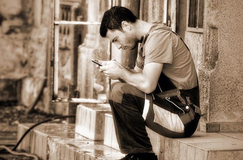 A man sitting and looking down at his phone, hunched over