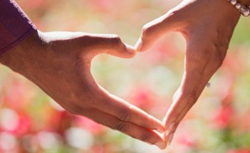 A couple's hands forming a heart with a blurry background