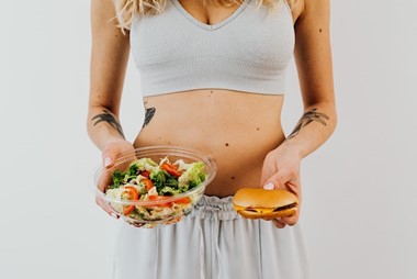 A woman holding a salad and a cheeseburger side by side