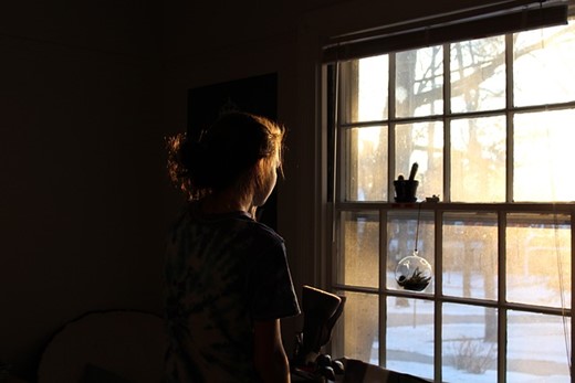 A woman standing in a dark room, looking out onto a cold morning