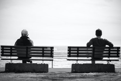 two men sitting on benches facing the water