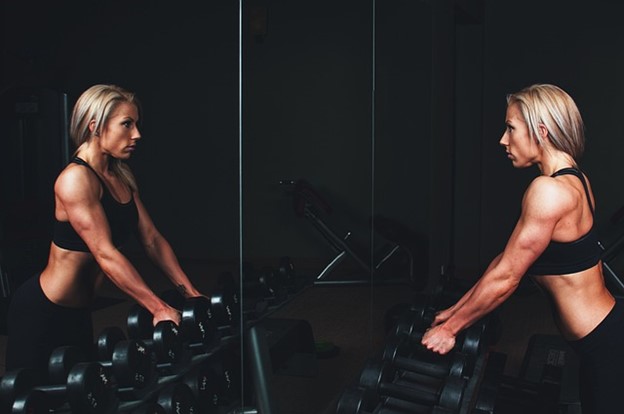 A determined woman looking at herself in the mirror while lifting weights