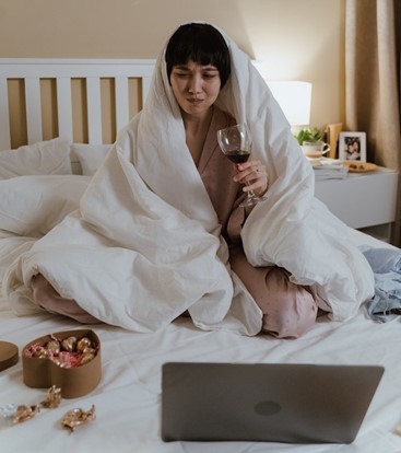 a woman drinking wine, eating chocolate, and watching TV in bed