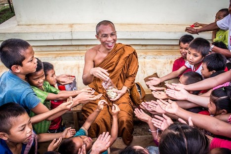 a smiling Buddhist monk giving popcorn to a bunch of children