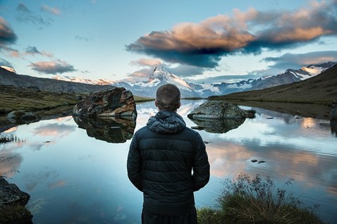 A man looking upon a lake with mountains in the background