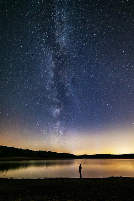 a person standing on a lake shore looking up at the Milky Way