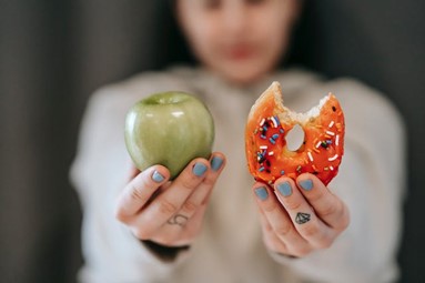 a person holding up two choices: an apple and a donut