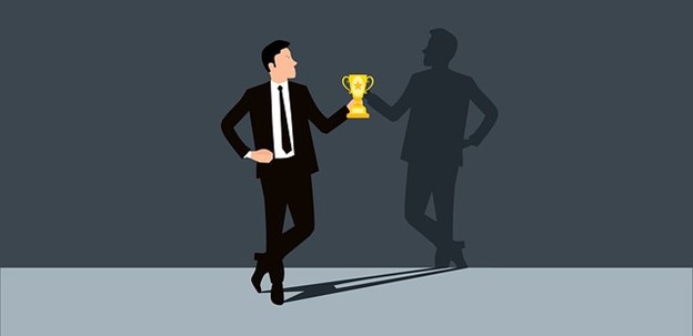 A man holding a trophy while looking at his shadow on the wall.