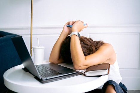 a woman in front of a laptop with her head down, looking frustrated