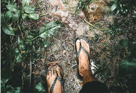 a man walking a muddy trail in flip flops