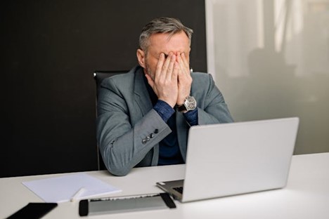 An upset man covering his face with his hands at his desk
