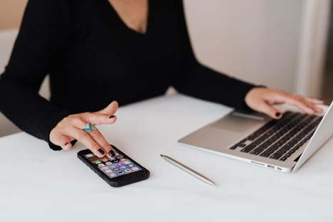 a woman touching the homescreen of her phone while working on a laptop