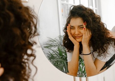 a young woman looking in the mirror with self-doubt