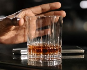 a hand reaching for a whiskey glass